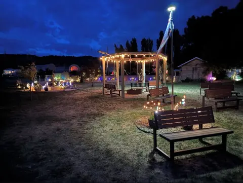 A lit gazebo and benches in a grassy area at dusk.