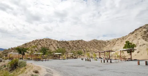 A gravel picnic area with covered tables set against arid hills under a cloudy sky.