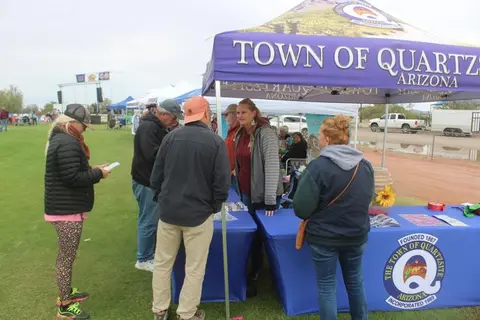 People gather at a town information booth outdoors on a grassy area.
