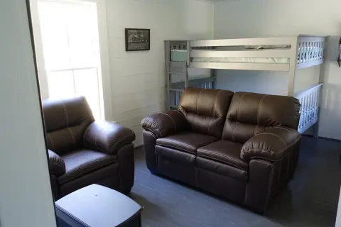 An interior room with a bunk bed, brown leather sofa, and armchair.