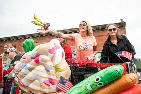 People ride on a decorated float and throw snacks into a crowd.