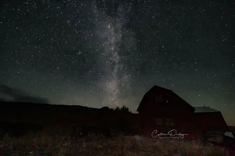 A night sky full of stars above a dark building and hills.
