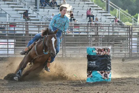 A rider on a horse rounding a barrel during a rodeo event.