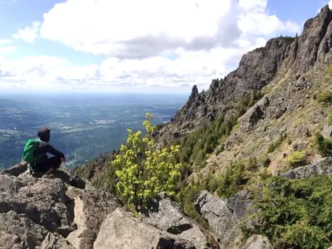 A person looks out over a landscape from a rocky mountain peak.