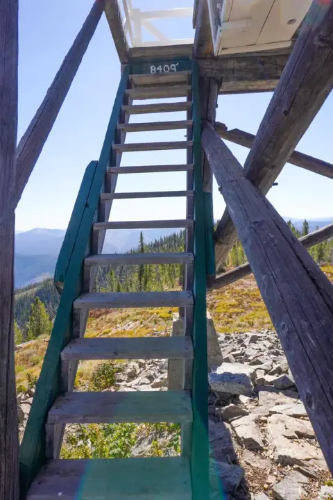 A wooden staircase leads up a tower structure with a mountain landscape in the background.