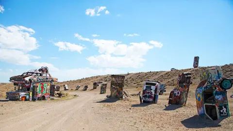 A row of cars planted vertically in the desert ground, covered in graffiti.