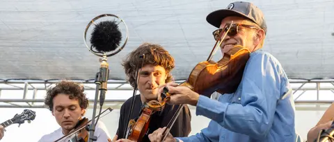 A band playing string instruments outdoors near a microphone.