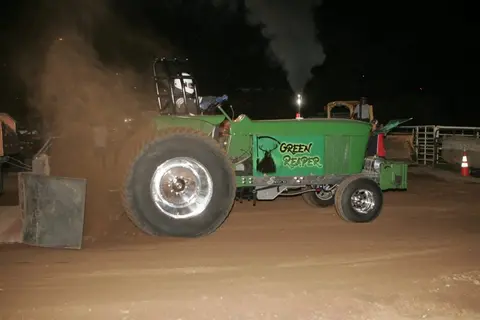 A modified green tractor participates in a tractor pull event.