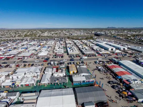 An aerial view shows a sprawling outdoor market with many tents, RVs, and vehicles.