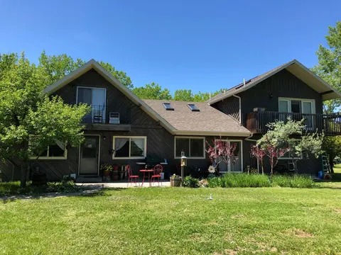 A two-story dark wood house with a lawn and trees in front.