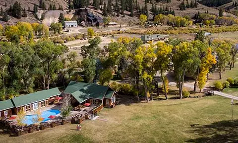 An aerial view of cabins and a swimming pool nestled in a valley with autumn trees.