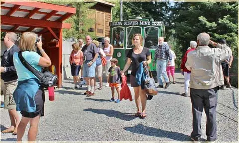 A group of tourists gather outside near a green vehicle labeled for a mine tour.