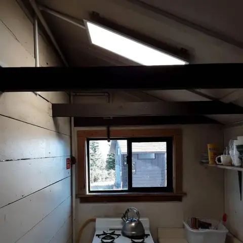 An interior view of a rustic cabin showing a window, stove, and exposed beams.