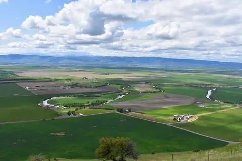 An aerial view of a wide valley with meandering rivers and farmlands under a cloudy sky.