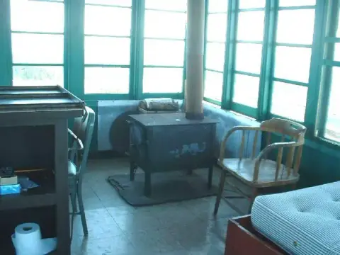 An interior view of a room with green-framed windows, a wood stove, and a wooden chair.