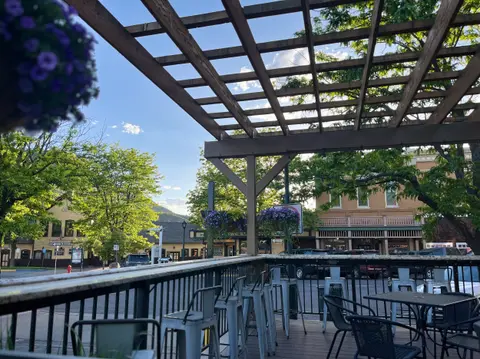 An outdoor patio view with a wooden trellis, bar stools, and a street scene in the background.