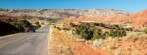 A car drives along a road through a desert landscape with red rock formations.