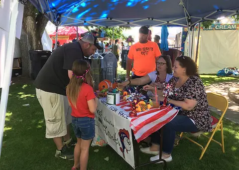 People at a festival booth under a tent.