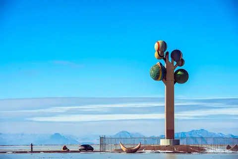 A tall colorful tree-like sculpture stands in a desert landscape under a blue sky.