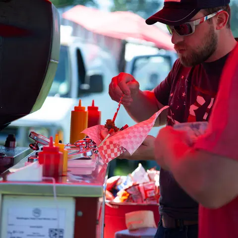 A man adds sauce to food at an outdoor food stand.