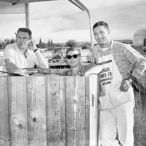 A historic photograph showing three men at a wooden stand outdoors.