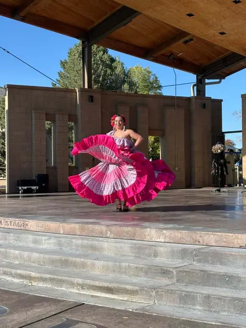 A woman dances on an outdoor stage in a large pink ruffled dress.