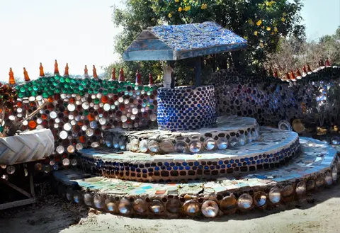 A wishing well structure made of glass bottles and mosaic tiles.