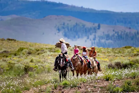 A group of people horseback riding through a mountain landscape.