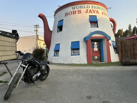A motorcycle is parked in front of a quirky coffee shop shaped like a giant teapot.