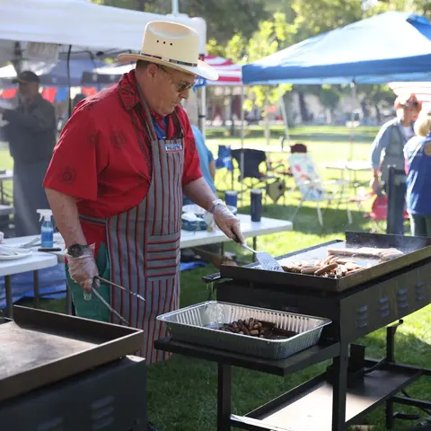 A person wearing a cowboy hat and apron grills food outdoors.