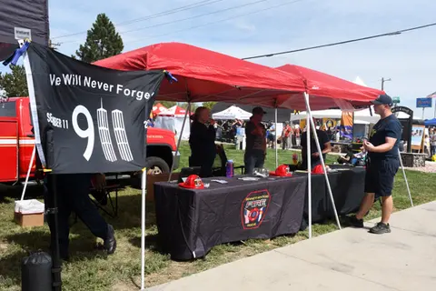 People stand behind a fire department booth with a 9/11 memorial flag outdoors.