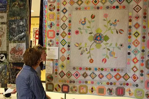 People looking at a large colorful quilt hanging at an exhibition.