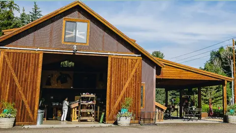 An exterior view of a large wooden barn with open doors showing an interior shop.