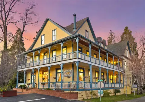 Exterior view of a large multi-story yellow building with wraparound porches at dusk.
