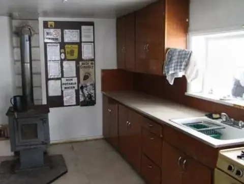 A photograph of the interior of a cabin kitchen featuring a wood stove and sink.
