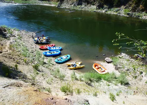 Several colorful rafts are pulled up on the rocky bank of a river.