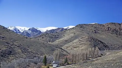 A landscape view of mountains with snow-capped peaks and a small building in a valley.