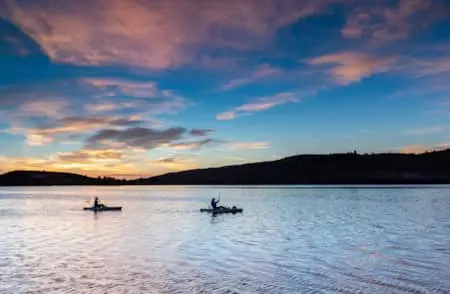 Two people kayaking on a calm body of water during a scenic sunset.