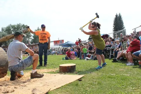 A woman prepares to swing an axe at a block of wood during an outdoor competition.