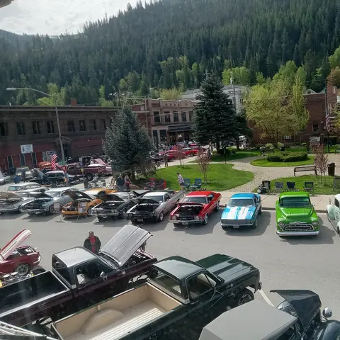 An elevated view of a classic car show in a town square with forested mountains in the background.