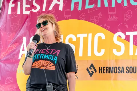 A woman wearing sunglasses speaks into a microphone in front of a banner.