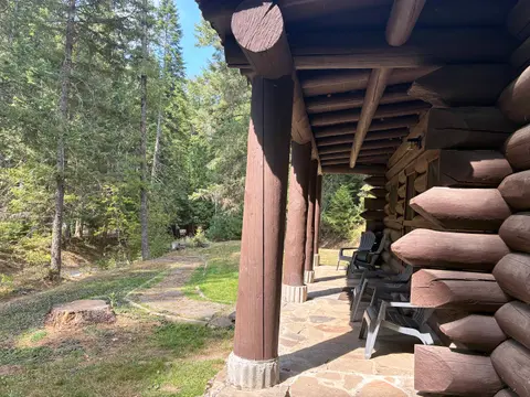 A rustic log cabin porch looks out onto a forested path.