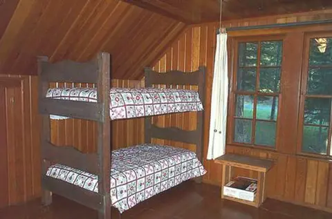 A wooden bunk bed stands inside a rustic room with wood-paneled walls and ceiling.