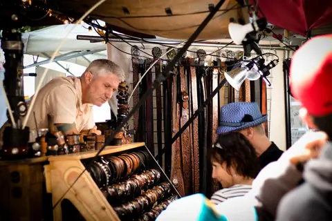 A vendor tends to a leather goods stall at an outdoor market.