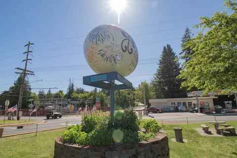 A large decorated egg monument stands outdoors near a street under a bright sun.