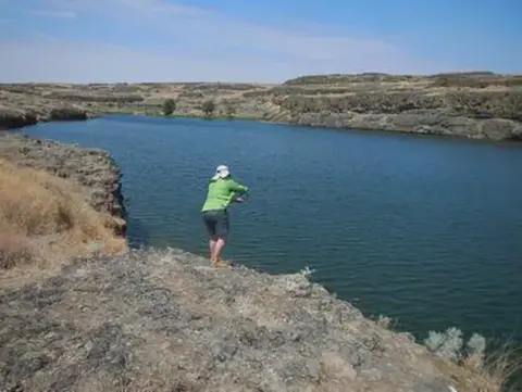 A person fishes from a rocky bank by a lake.
