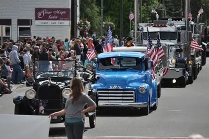 A crowd watches a parade with vintage cars and large trucks on a street.