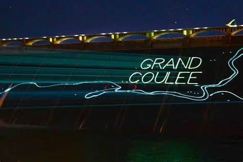 A night view of a large dam illuminated with light projections.