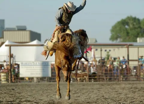 A cowboy rides a bucking horse at a rodeo event.
