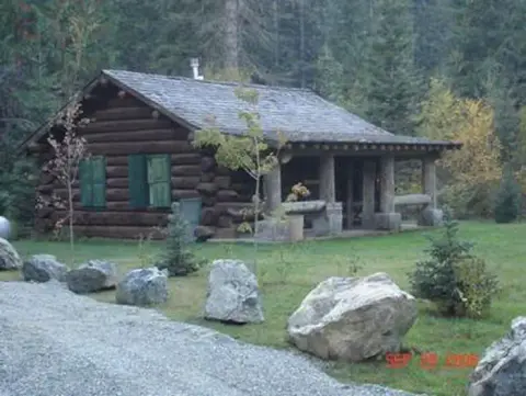 A log cabin surrounded by trees and large rocks.